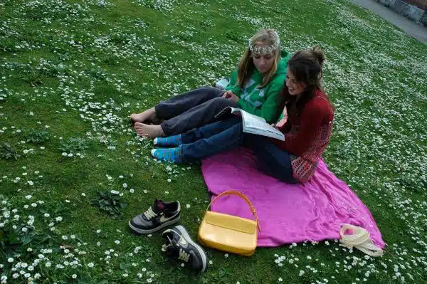 Girls reading a book in a field of daisies, one wears a daisey chain crown, Seattle, Washington, USA