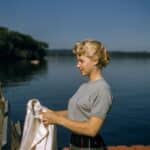 woman holding white textile standing beside body of water