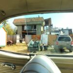 Through the window of a vintage automobile, a view of Fairbanks neighborhood, storage building, burned out house, do it yourself renovations with no permit required, truck, fence, Alaska, USA