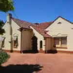 Adelaide. 1940s Art Deco house. Stucco walls, decorative chimney, stepped bricks on corners and chimney, rounded window ridge, rounded porch entry leadlight window, glazed bricks above foundations, asymmetrical facade .