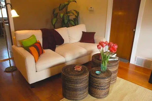 Peggy's Zen living room makeover, white sofa, pink tulips, bright pillows, maroon throw, natural woven drum shaped tables, jute rug, refinished floor, old brass floor lamp, Seattle, Washington, USA