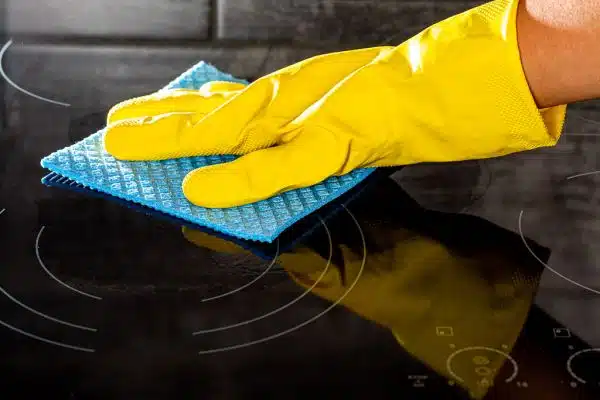 Woman's hand in a yellow rubber glove cleans the shiny electric hob. The concept of cleaning and homework