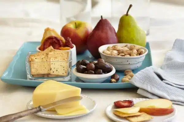 sliced cheese apples pears dried peaches prunes apple pistachios chocolate covered almonds crackers on blue ceramic tray with cloth towel napkin