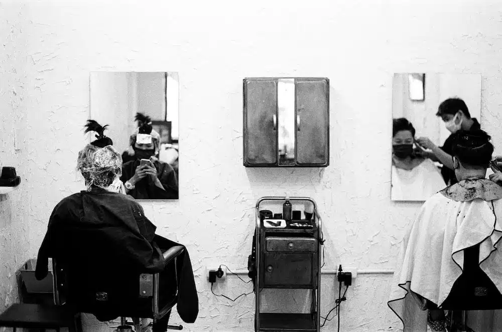 a black and white photo of a woman getting her hair cut