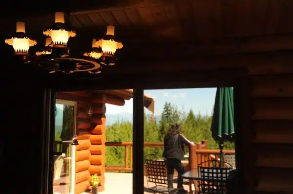 A neighbour standing on the deck taking in the view, wagon wheel lamp, patio furniture, through the sliding glass doors at Auntie's log cabin, Alderbrook Golf Course, Union, Washington, USA