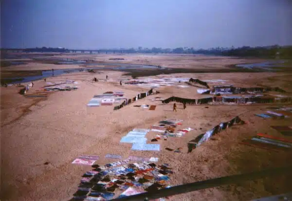 Close up wallas washing clothes, saris, sheets and bedding in a river and hanging them to dry, from a Buddhist pilgrimage tour bus, on a bridge, town, Northern India, 1993