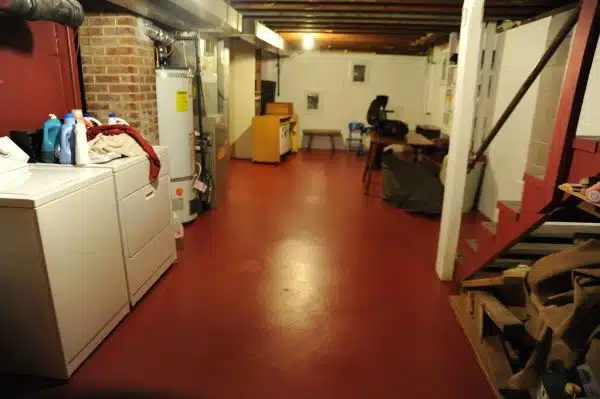 Freshly painted basement floor, clean clothes, rafters, brick chimney, washer and dryer, water heater, central heating system, tables, rolled up carpets, sawhorses, staircase, Wedgwood, Seattle, Washington, USA